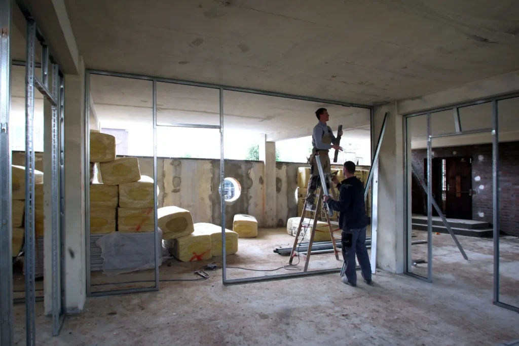 Two workers install metal framing in an unfinished building interior.