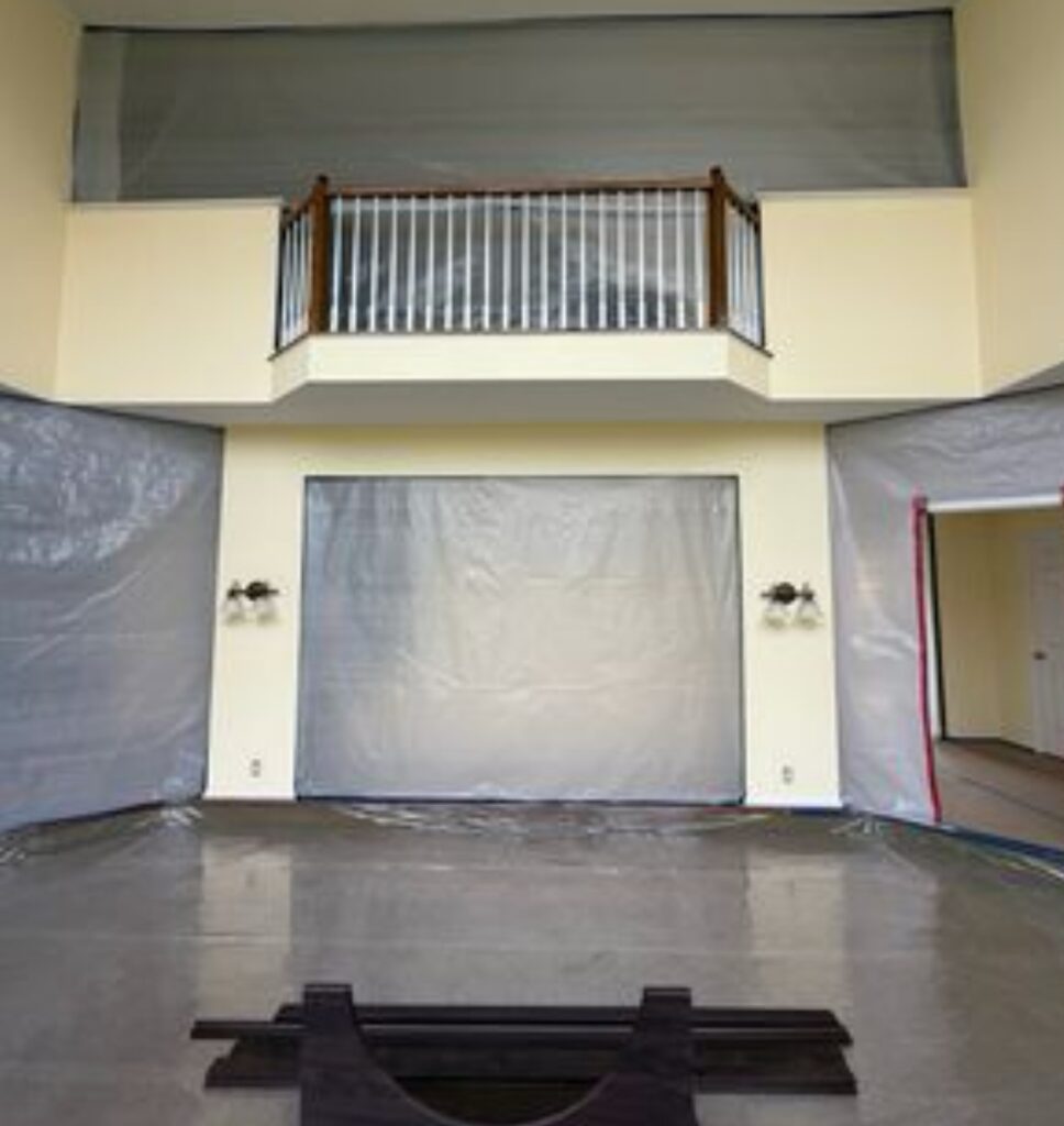 Indoor space with plastic-covered walls and a balcony with wooden railing above.